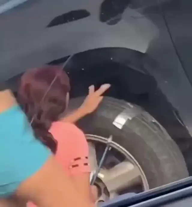 Девушка в голубом топе наматывает и приклеивает серебристый скотч поверх автомобильной покрышки и диска — девушка в розовой футболке, девушк
