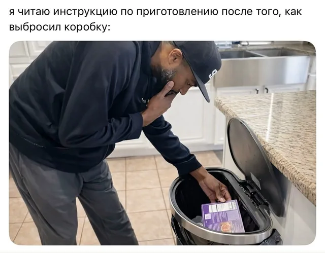 Мужчина наклонился над мусорным ведром и достает оттуда фиолетовую коробку с едой — мужчина в черной толстовке и кепке