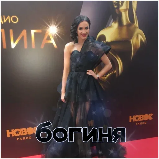 Статичное фото, женщина позирует фотографам на мероприятии. — женщина в черном вечернем платье