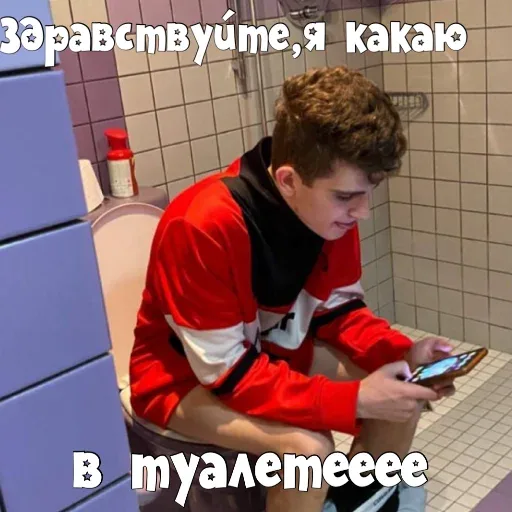 Парень сидит на унитазе, держа в руках телефон — молодой человек в красной кофте