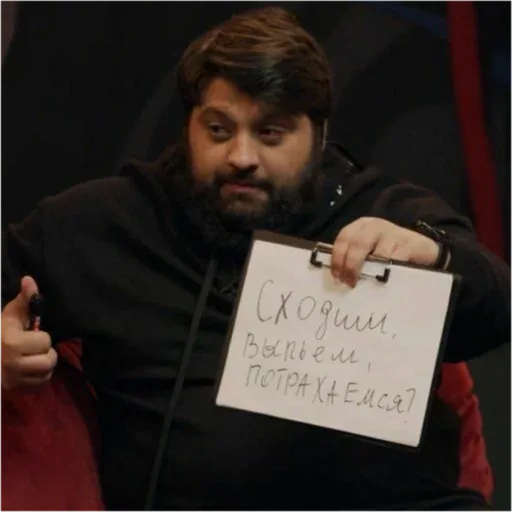 Тамби Масаев показывает планшет с надписью в камеру, при этом большой палец другой руки поднят вверх в жесте одобрения. — Тамби Масаев
