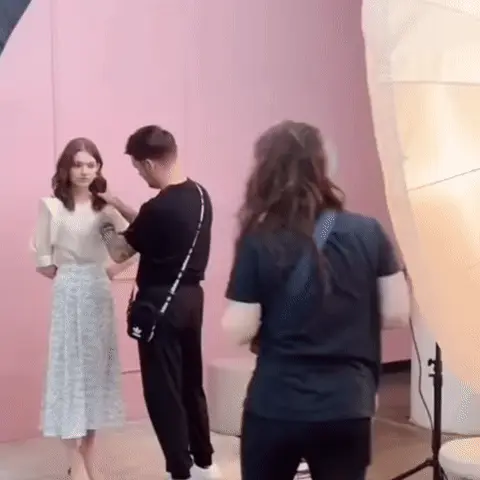 Стилист постоянно поправляет волосы модели, модель стоит неподвижно, фотограф делает кадры. — модель с нейтральным выражением лица