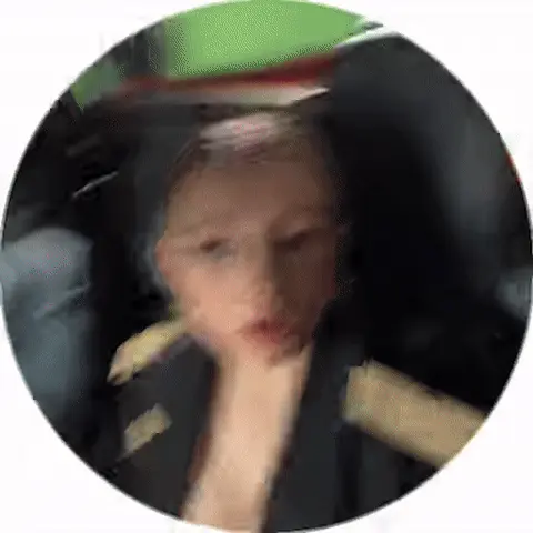 Полина сидит неподвижно, глядя в камеру, в то время как парень на заднем плане слегка двигается, создавая эффект случайного присутствия в ка