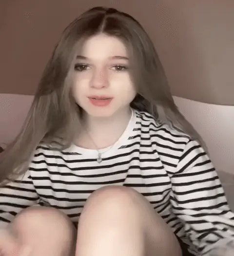 Девушка ритмично соединяет пальцы рук, образуя форму сердца, и слегка покачивается в такт. — девушка с длинными волосами в полосатой кофте