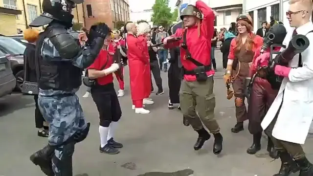 Косплееры персонажей Team Fortress 2 и человек в экипировке силовика ОМОНа синхронно танцуют казачок на улице