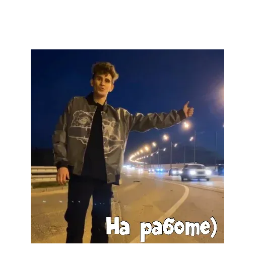 Парень стоит на обочине и держит руку поднятой для остановки попутной машины. — молодой парень с укладкой в куртке