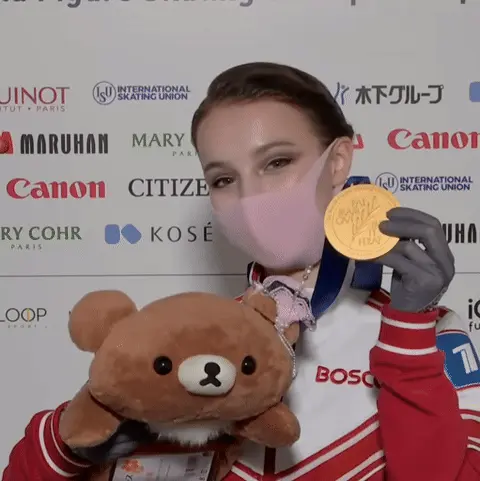 Девушка держит перед собой медаль и игрушку, слегка покачивая головой в такт зацикленному движению.