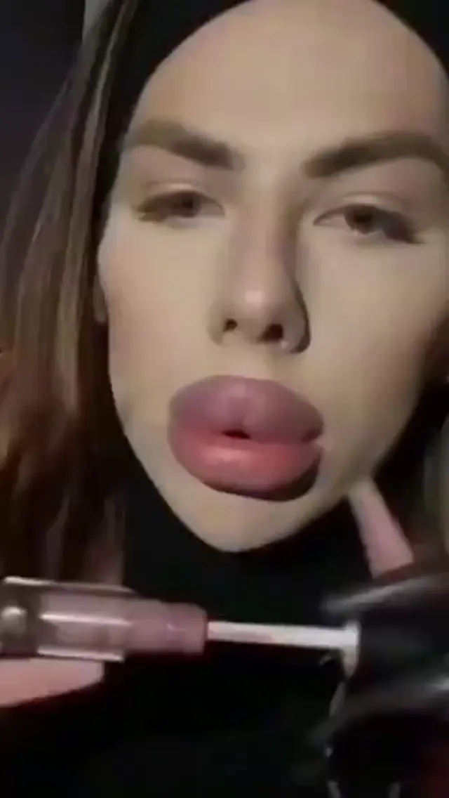 Женщина красит массивные губы блеском, затем видео сменяется кадром, где другая женщина подносит к лицу сосиски на малярном валике, после че