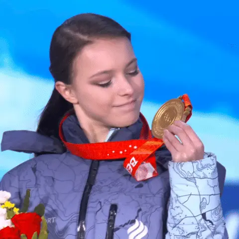 Девушка рассматривает медаль в руке, затем слегка улыбается и переводит взгляд.