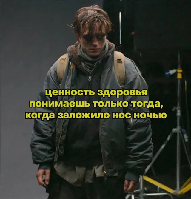 Изможденный мужчина в куртке и с рюкзаком стоит с понурым видом, глядя вниз — Роберт Паттинсон (в роли Брюса Уэйна из фильма «Бэтмен»)
