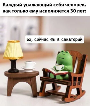 Лягушка сидит в кресле, держа в руках чашку и книгу, имитируя уютный домашний отдых.