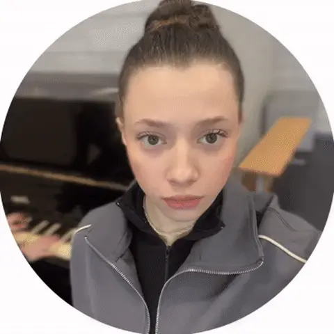 Девушка стоит перед камерой, на фоне человек играет на пианино, она делает медленное движение глазами (закатывает их или моргает) в такт муз
