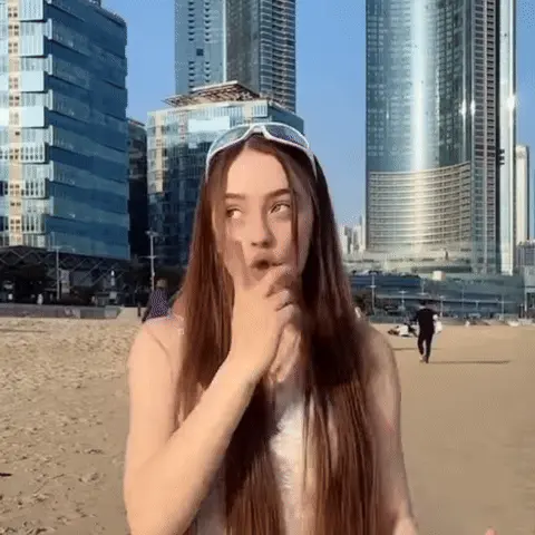 Девушка ритмично подносит палец к губам и слегка отводит его, создавая эффект зацикленного жеста «тсс» или раздумья. — девушка с длинными во