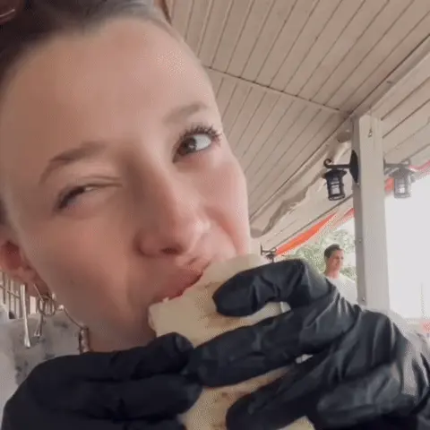 Девушка откусывает кусок шаурмы, жует, глядя в камеру, и снова подносит еду ко рту в зацикленном движении. — Полина Гухман, девушка с собран