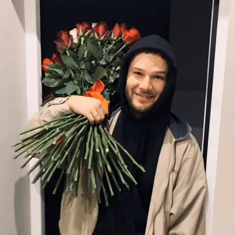 Макс Корж стоит с букетом, слегка покачиваясь в кадре, улыбка остается неизменной. — Макс Корж