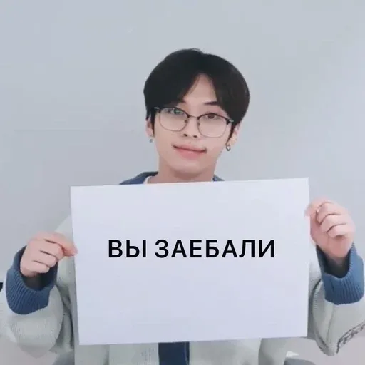 Человек держит лист с надписью на уровне груди, демонстрируя его зрителю. — молодой человек в очках
