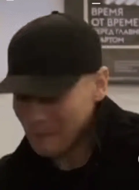 Человек прикрывает рот рукой, пытаясь скрыть смех, затем убирает руку и улыбается. — SHAMAN (Ярослав Дронов)