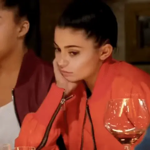 Kylie Jenner сидит неподвижно, изредка слегка меняя направление взгляда, сохраняя одну и ту же позу скуки.