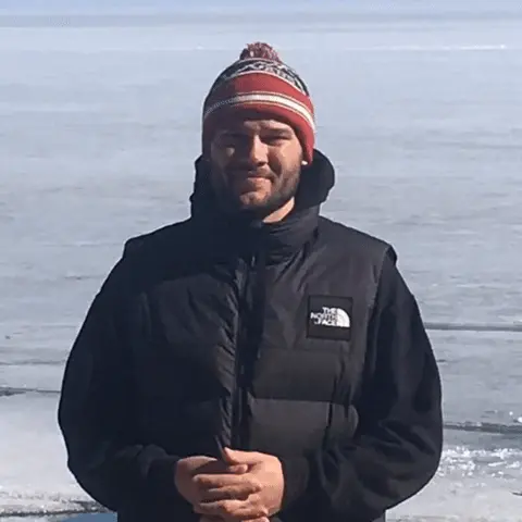 Мужчина стоит на месте, слегка покачиваясь, руки сложены перед собой в районе живота. — мужчина в красной шапке и черном жилете