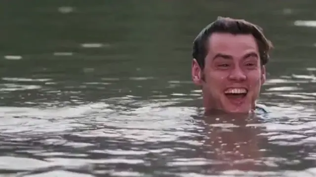 Джим Керри весело смеётся в воде, перед ним выныривает крокодил и резким броском нападает с брызгами — Джим Керри