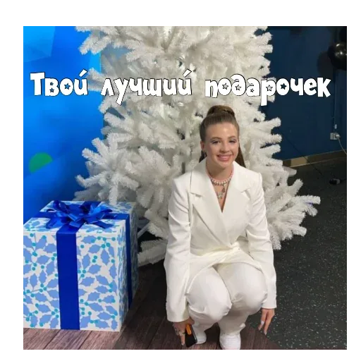 Девушка позирует для фото, присев рядом с новогодним декором. — девушка в белом костюме