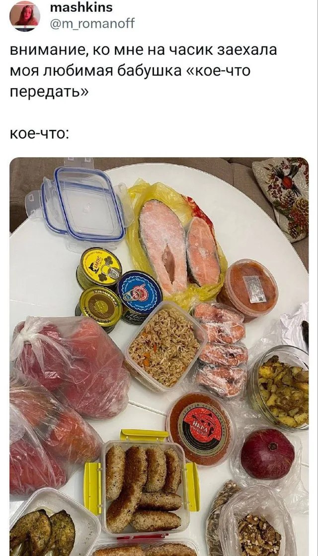 На столе разложено огромное количество еды: два куска красной рыбы, банки консервов, контейнеры с котлетами, салатом, икрой, соленьями, паке