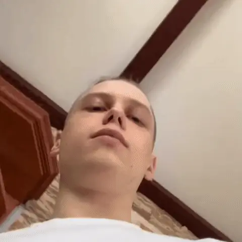 Парень смотрит в камеру, затем поднимает руку и прикладывает указательный палец к губам, призывая к тишине. — молодой парень в белой футболк