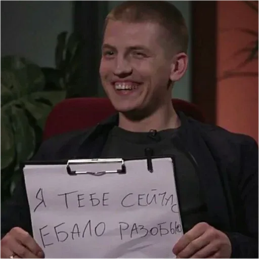 Человек держит планшет с угрожающей надписью, при этом сам улыбается, создавая контраст между текстом и мимикой. — Алексей Щербаков