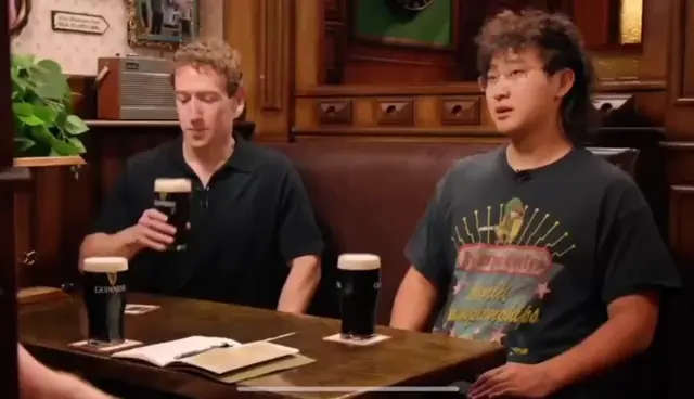 Марк Цукерберг поднимает бокал Guinness, делает глоток и отводит взгляд, сохраняя роботоподобное спокойствие, пока парень рядом жестикулируе