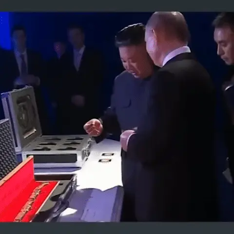 Ким Чен Ын делает короткое движение рукой над столом, Владимир Путин наблюдает за этим, оба стоят рядом и изучают содержимое кейсов. — Влади
