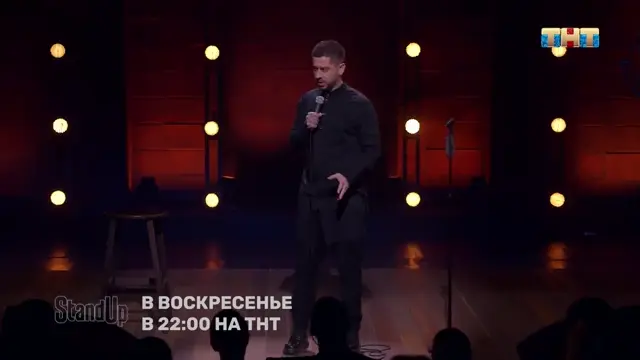 Комик стоит на сцене, жестикулирует свободной рукой, держит микрофон, произносит монолог и в финале слегка отводит руку в сторону