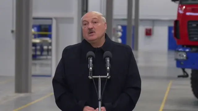 Лукашенко стоит за микрофонной стойкой, произносит речь и делает приглашающий жест правой рукой в сторону. — Александр Лукашенко