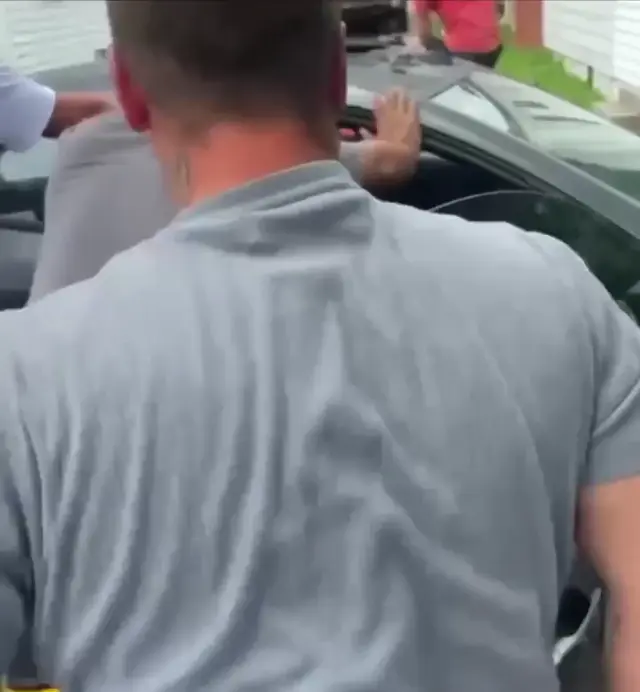 Несколько мужчин подхватывают боковую часть автомобиля, раскачивают и толчком переворачивают его кверху колёсами. — группа мужчин во дворе