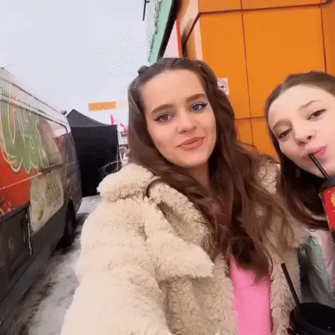 Девушка слева ведет съемку и говорит, девушка справа пьет из стакана, а затем внезапно делает «упоротое» лицо, глядя в сторону или на камеру
