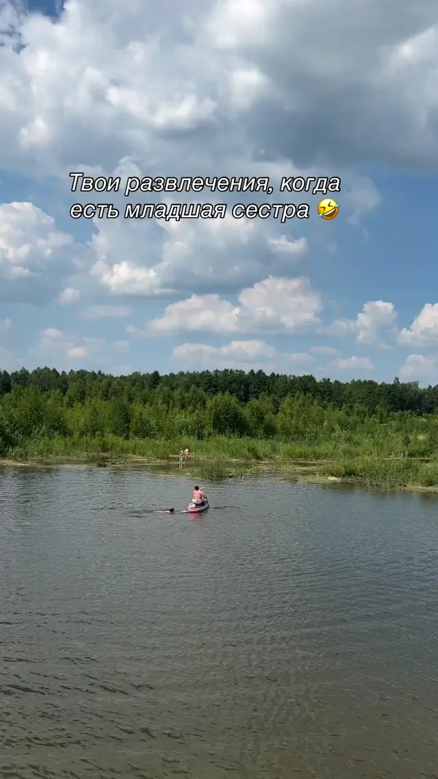 Мужчина спокойно сидит на сапборде, девушка встает, начинает раскачивать доску и прыгает в воду, из-за чего мужчина падает в озеро вместе с 