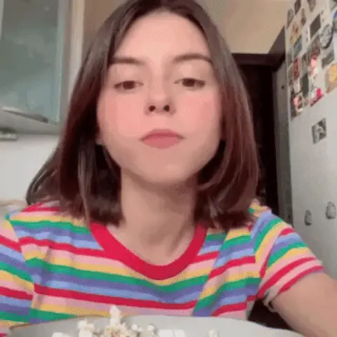Девушка ест попкорн, глядя в камеру, затем меняет выражение лица на скептическое. — Дора