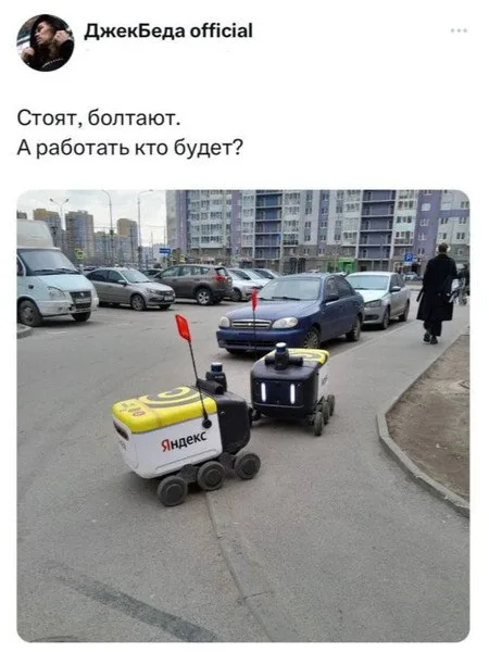 Два робота стоят неподвижно на асфальте, имитируя диалог двух людей.