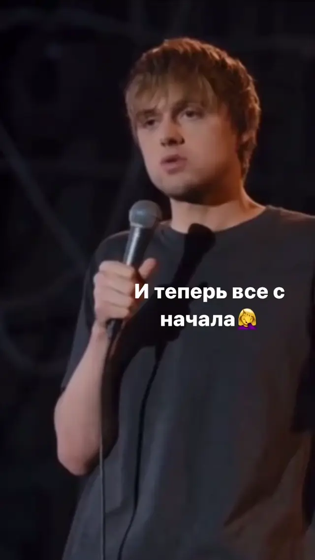 Комик держит микрофон на стойке, говорит монолог на сцене и слегка жестикулирует свободной рукой — Ваня Усович