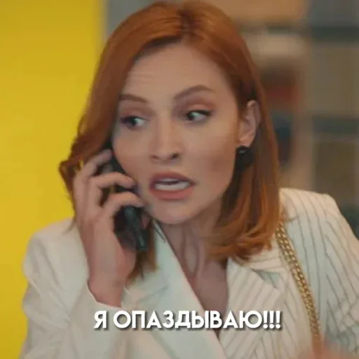 Женщина держит телефон у уха и говорит, активно жестикулируя или выражая эмоции лицом. — женщина с рыжими волосами в белом пиджаке